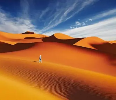 a person walking on a sand dune in the desert at desert camp sahara luxury in Merzouga