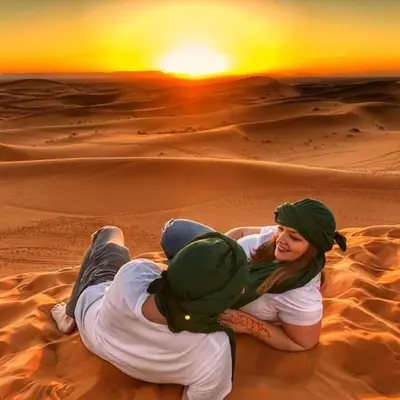 a woman sitting on the sand in the desert at Auberge Tigida in Mhamid