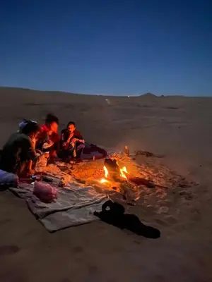 a group of people sitting around a fire in the desert at Auberge Tigida in Mhamid