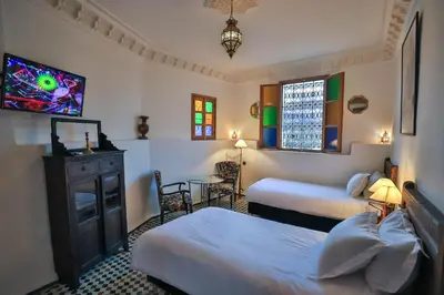 a bedroom with two beds and a tv and a table at Riad Soultana in Fès