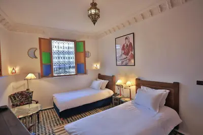 a bedroom with two beds and a chair and a window at Riad Soultana in Fès