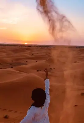 a woman flying a kite in the desert at sunset at Merzouga cheer camp in Merzouga