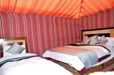 a room with two beds in a red wall at Merzouga cheer camp in Merzouga