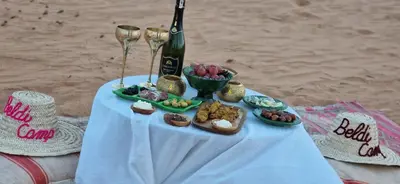 a table with a bottle of wine and a plate of food at Beldi camp in Merzouga