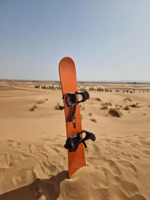 an orange snowboard sitting in the sand in the desert at Beldi camp in Merzouga