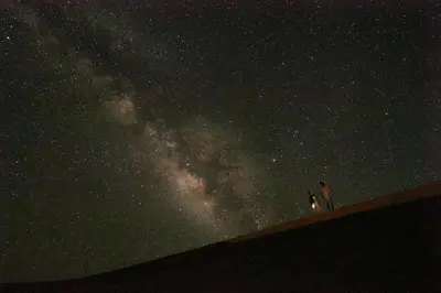 two people standing on a wall looking at the milky way at Beldi camp in Merzouga