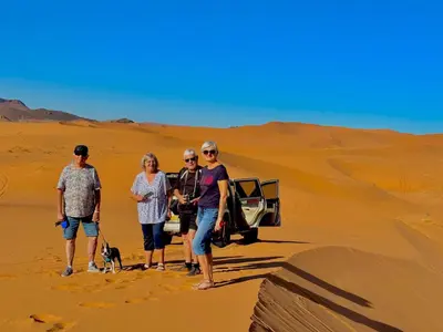three people and a dog walking in the desert at Porte De Sahara Ouzina in Ouzina