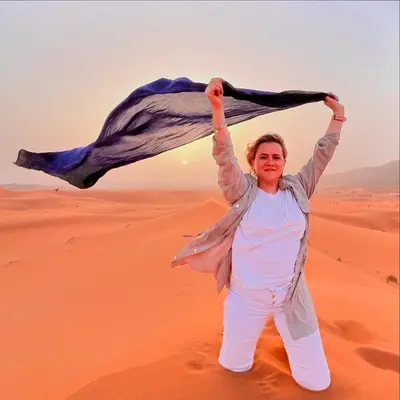 a woman in the desert holding up a scarf at Porte De Sahara Ouzina in Ouzina