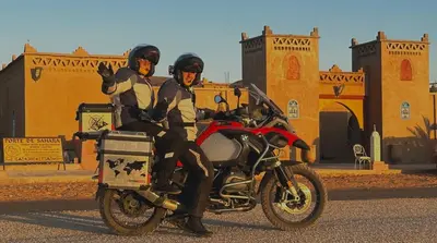 two people sitting on a motorcycle in front of a building at Porte De Sahara Ouzina in Ouzina