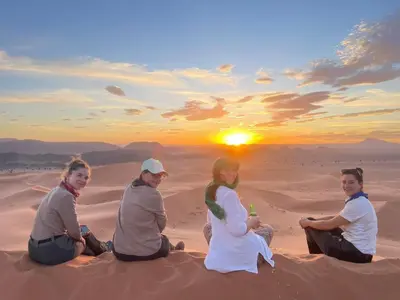 four women sitting in the desert watching the sunset at Porte De Sahara Ouzina in Ouzina