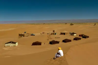 a man sitting in the middle of a desert at Atta Desert Camp in El Gouera