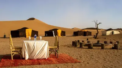 a table in the middle of a desert with tents at Atta Desert Camp in El Gouera