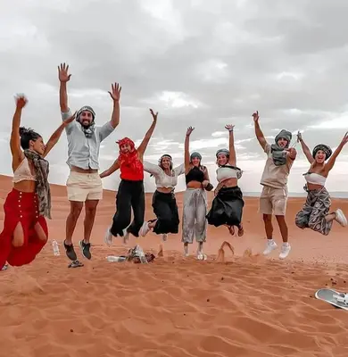 a group of people jumping in the air on the beach at Sahara Luxury Tented Camp in Merzouga