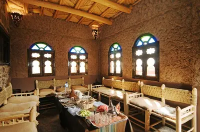 a dining room with tables and chairs and windows at Tigmi Tachddirt in Tacheddirt