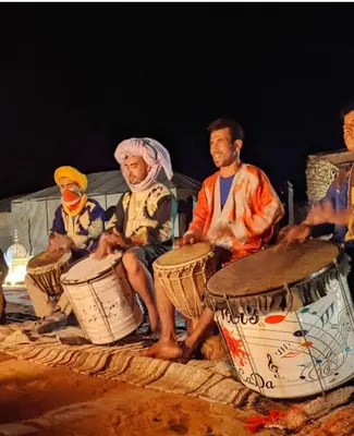 a group of people playing drums on the beach at Golden Camel Desert Camp - Merzouga Luxury Camp in Merzouga