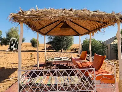 a straw umbrella with chairs and a table in the desert at Tafouyte Luxury Camp in Merzouga