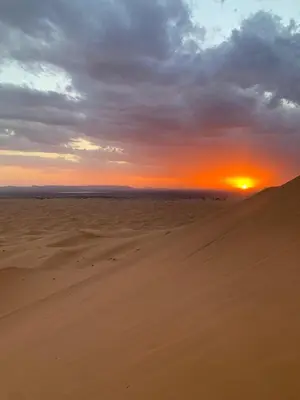 a sunset in the desert with a sand dune at Tafouyte Luxury Camp in Merzouga