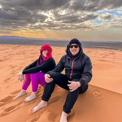two people sitting on the sand in the desert at Desert Lover's Luxury Camp in Merzouga