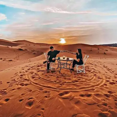 a man and a woman sitting at a table in the desert at Desert Lover's Luxury Camp in Merzouga