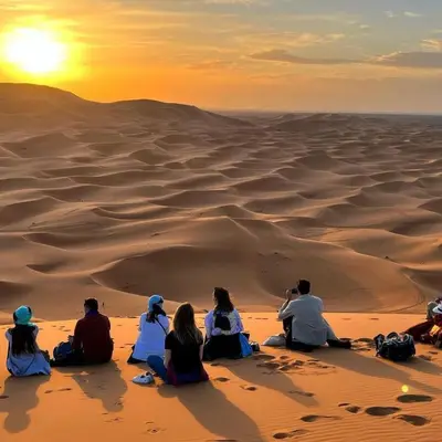 a group of people sitting in the desert watching the sunset at Desert Lover's Luxury Camp in Merzouga
