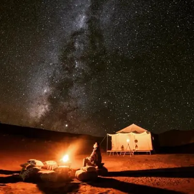 a man sitting in front of a tent under the stars at Desert Lover's Luxury Camp in Merzouga