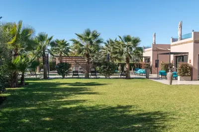 a lawn with palm trees in front of a house at Les Iris - Peaceful villa with heated private pool & hammam in Marrakech