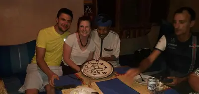 a group of people sitting around a table with a birthday cake at La Fibule D'or in Aït Ben Haddou