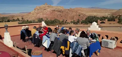 a group of people sitting at tables in front of a mountain at La Fibule D'or in Aït Ben Haddou