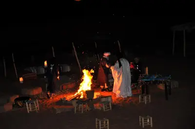 a group of people standing around a fire at night at Tuareg Luxury Camp in Merzouga