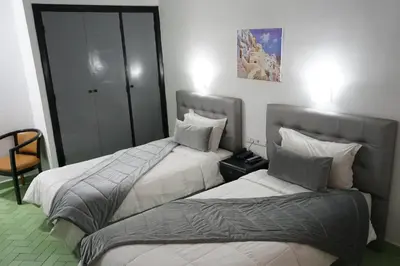 a hotel room with two beds and a chair at Hotel Nouzha in Fès