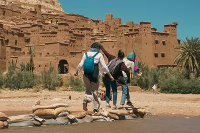 a group of people standing around a pile of animals in front of a castle at taman'art space in Aït Ben Haddou