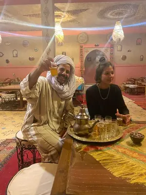 a man and a woman sitting at a table with a drink at Kasbah Azalay Merzouga takojt in Merzouga