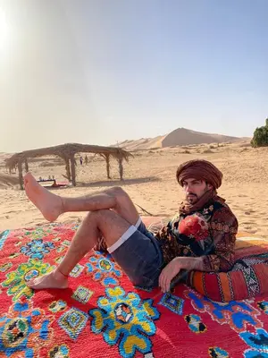 a man sitting on a blanket on the beach at Merzouga Glamping Camp in Merzouga
