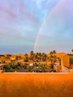 a rainbow in the desert with a parking lot at Hotel Riad Le Petit Prince in Merzouga
