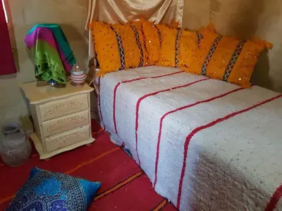 a bed with an orange and white blanket and a night stand at KASBAH Atlas-Aberdouz in Aït Hattab