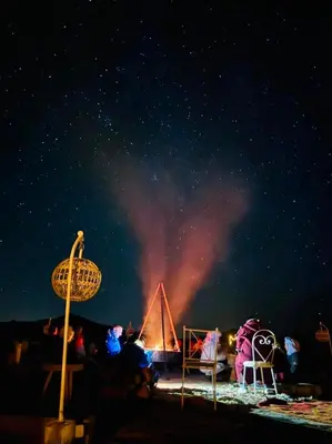 a group of people sitting around a fire at night at Starlit Luxury Camp in Merzouga