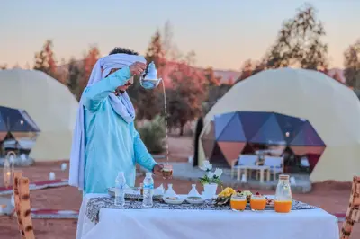 a woman standing at a table with a tea kettle at Merzouga Camel's & Camp in Merzouga