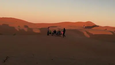 a group of people standing in the desert at sunset at Merzouga Camel's & Camp in Merzouga
