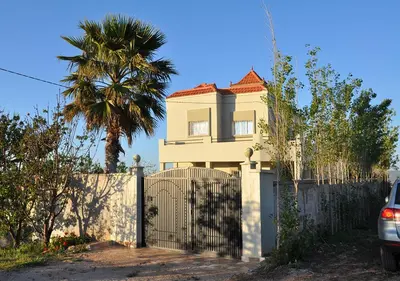 a white house with a fence and a palm tree at Vila Haja - Beautiful Farmhouse with a Private Pool! in Imouzzer Kandar