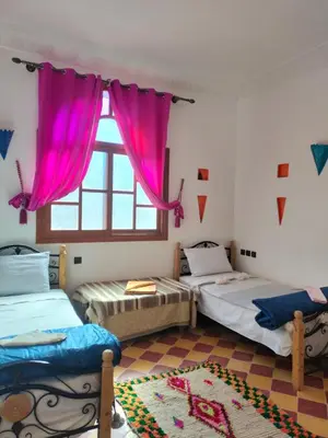 a room with two beds and a window with pink curtains at Riad dar Ahlam in Aït Baha