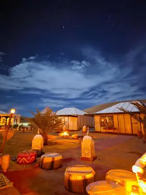 a building with a group of tables in front of it at night at Aladdin merzouga camp in Merzouga