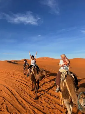 three people riding on camels in the desert at Aladdin merzouga camp in Merzouga