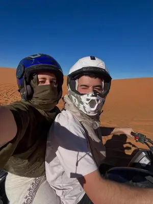 two men wearing helmets sitting on a motorcycle in the desert at Aladdin merzouga camp in Merzouga