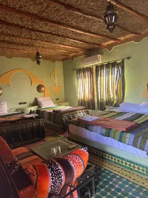 a room with three beds and a table and windows at AUBERGE KSAR MERZOUGA in Merzouga
