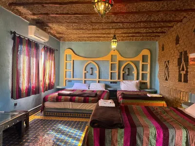 a bedroom with two beds and a table in it at AUBERGE KSAR MERZOUGA in Merzouga
