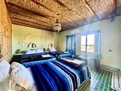 a bedroom with three beds and a window at AUBERGE KSAR MERZOUGA in Merzouga