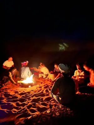 a group of people sitting around a fire on a beach at Desert Camel Trekking Camp in Hassilabied