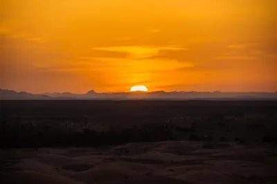 a sunset in the desert with the sun setting at Desert Camel Trekking Camp in Hassilabied