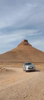 a car parked in the desert with a hill in the background at Bivouac ZAGORA in Zagora
