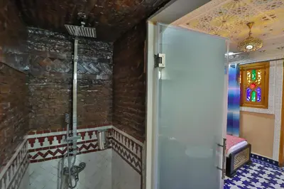 a bathroom with a walk in shower next to a brick wall at Hotel & Ryad DALILA in Fès